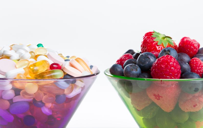 A bowl of vitamins next to a bowl of fruits Vitamins and Supplements