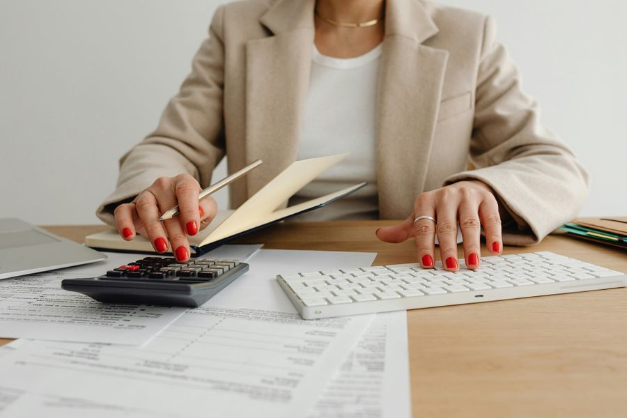 Close up of woman's hands with red nails working on financial documents with calculator Summit Salon Business Center Bookkeeping