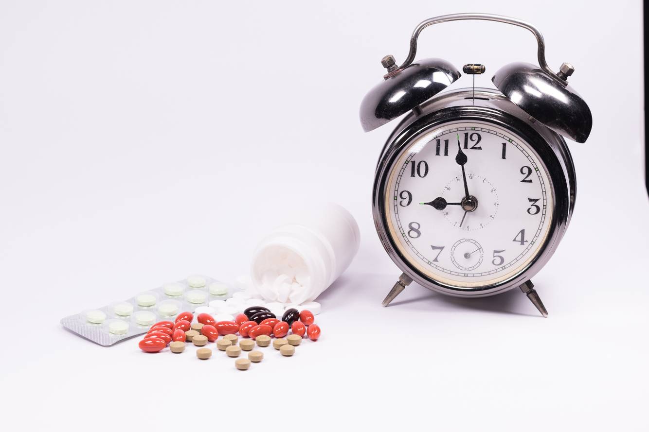 A clock and a variety of pills Medication Synchronization