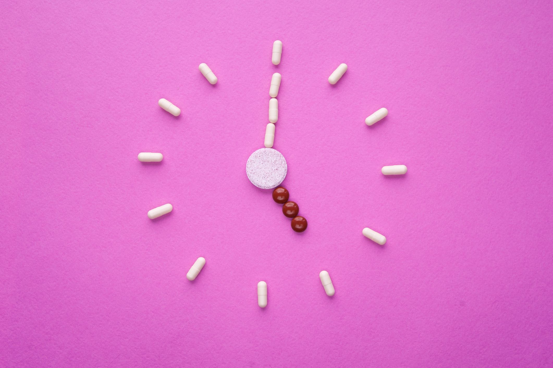 Pills in the shape of a clock on a pink background Med Sync