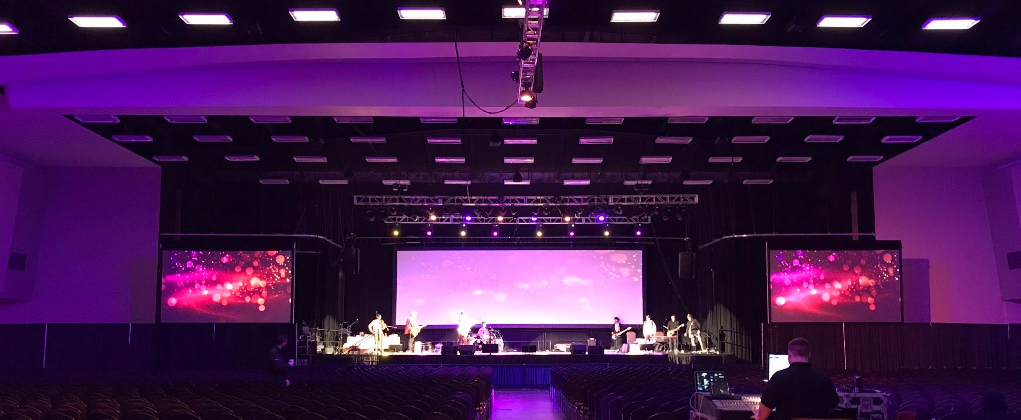 An image of a three-screen conference set up with pink lighting