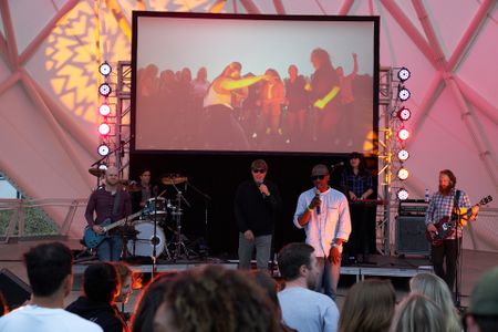 A band performing on stage with a projection display and LED lights 