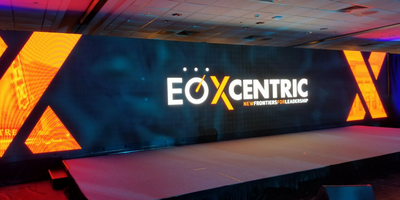 A large LED video wall displaying EO XCentric's logo