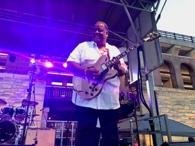 A man playing the guitar on a stage at a small outdoor concert