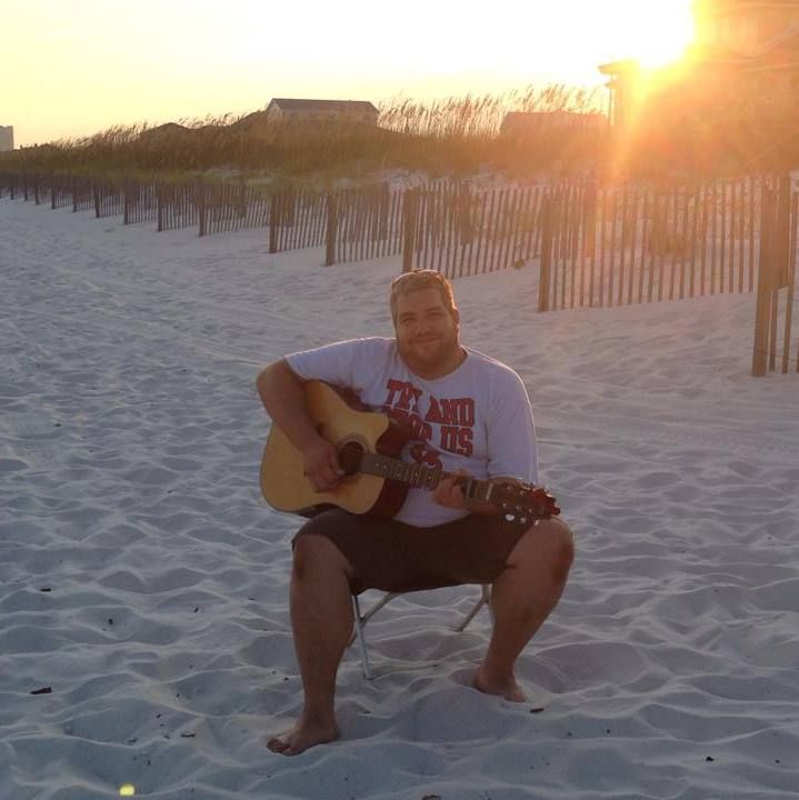 An image of Rob Burgess playing the guitar on a beach