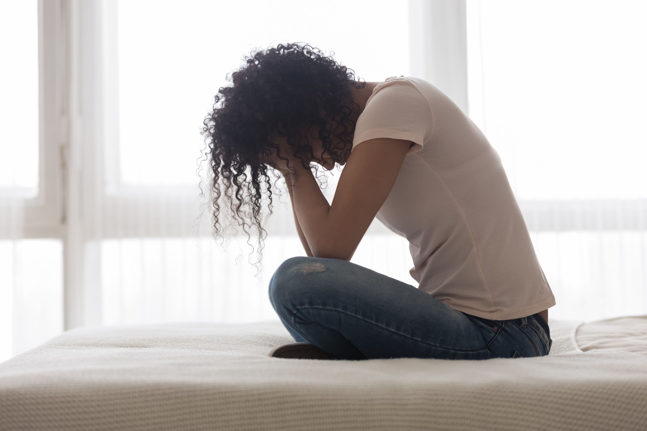 Woman sitting on her bed with her head down Trauma & Healing