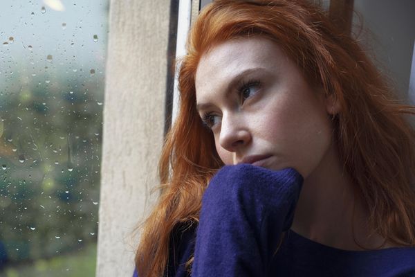 Woman sadly looking out a window on a rainy day 