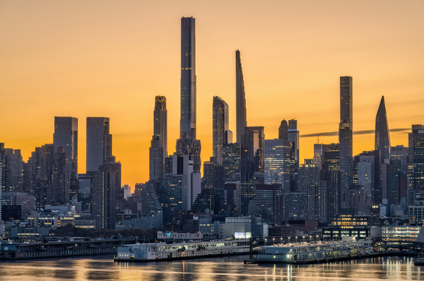 The New York City skyline at sunset, with a golden sky behind it and the Hudson river in the foreground.
