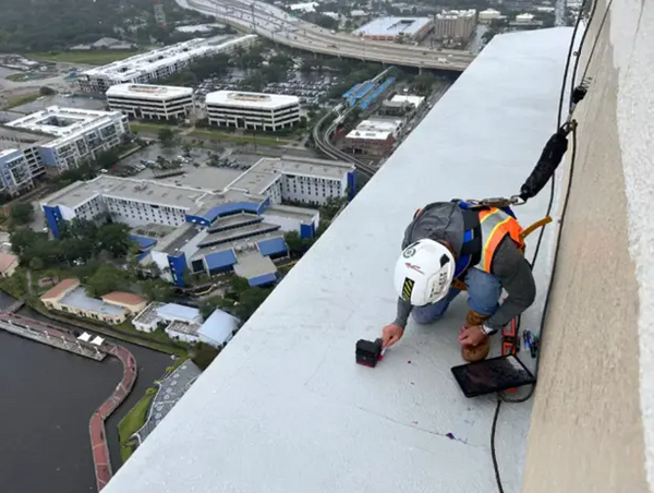 A GPRS Project Manager in full PPE and a harness scans concrete high above the Jacksonville, Florida skyline.