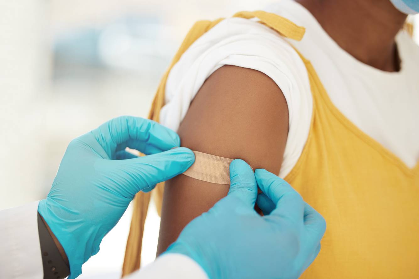 Woman getting a bandaid placed on her upper arm Vaccines