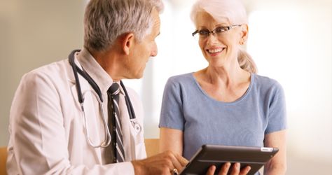 Doctor going over elderly woman`s health file in the office with tablet