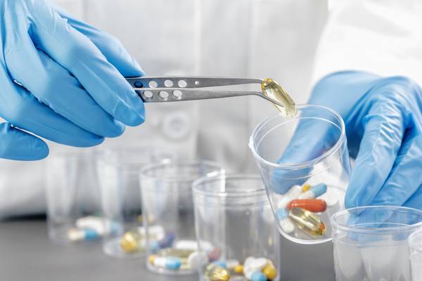 Doctor`s hand in blue gloves sorting with tweezers medication in glasses. Compounding