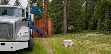 Container delivery truck moving through a wooded site with limited access