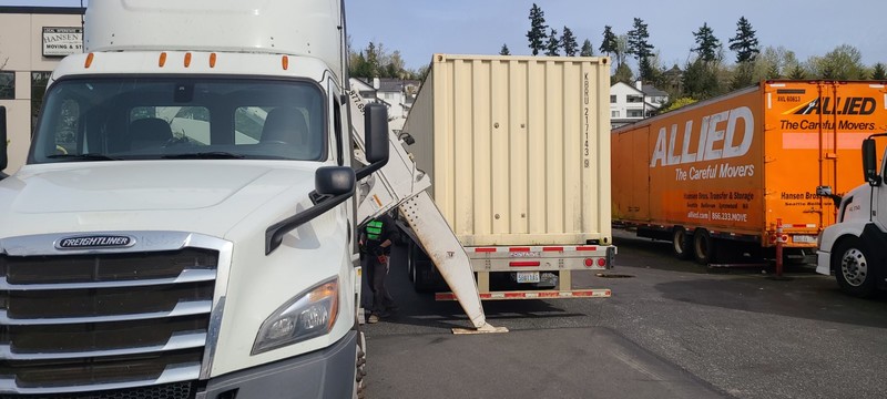 sideloader truck with support arms on the ground next to shipping container