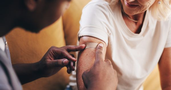 Image of an elderly woman being applied with a band-aid from a healthcare professional Immunizations