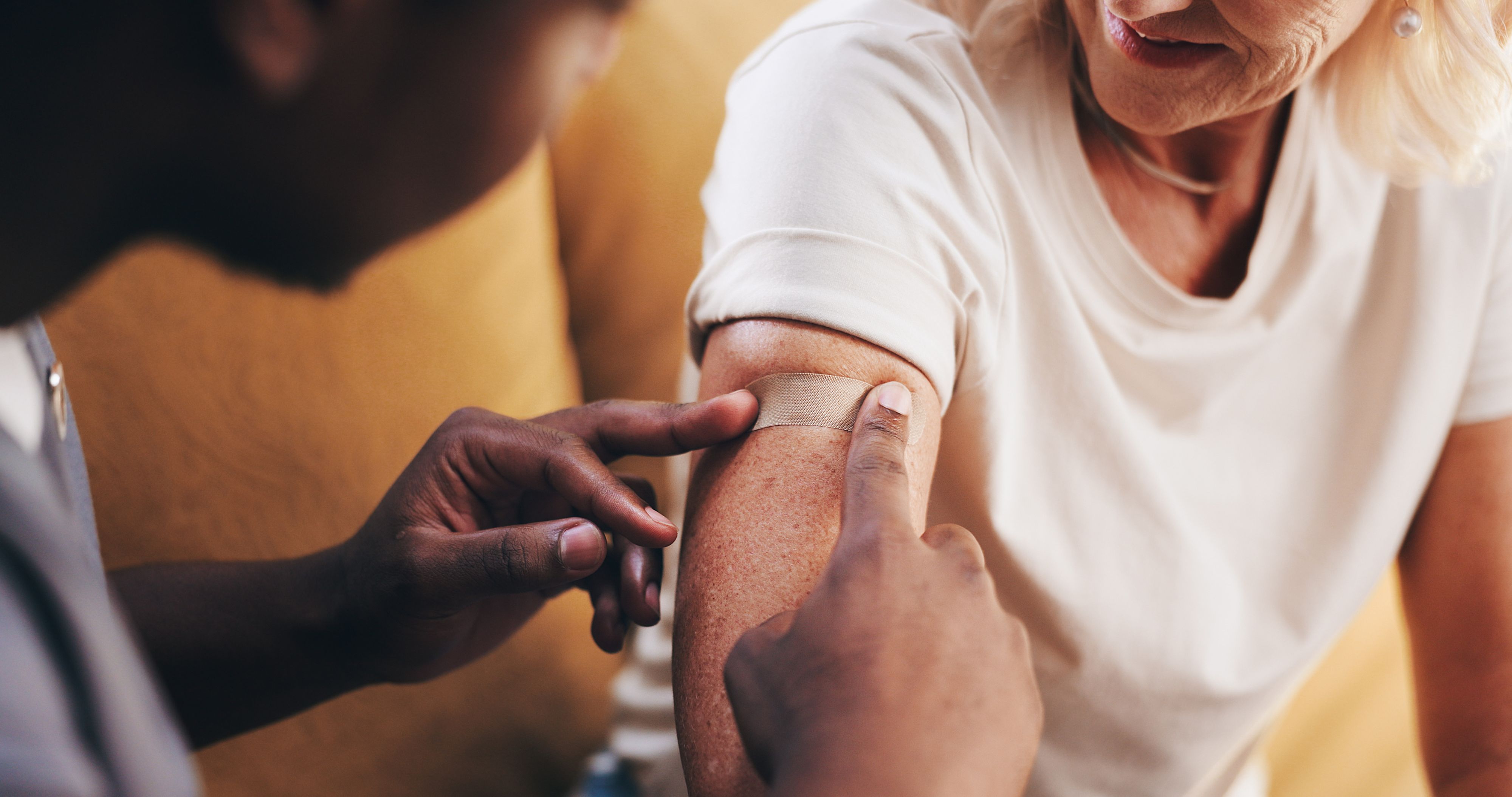 Image of an elderly woman being applied with a band-aid from a healthcare professional Immunizations