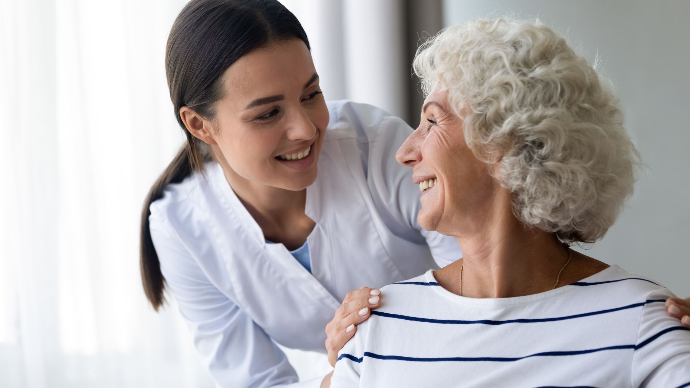 Picture of a woman provider holding the shoulders and smiling with an elderly woman patient Woman Provider and Patient
