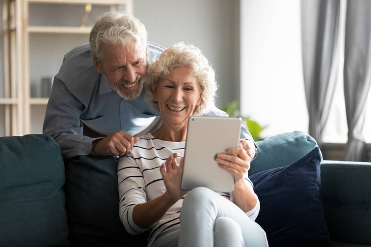 Happy senior couple sitting on a sofa and using a tablet for a telehealth appointment or video call.