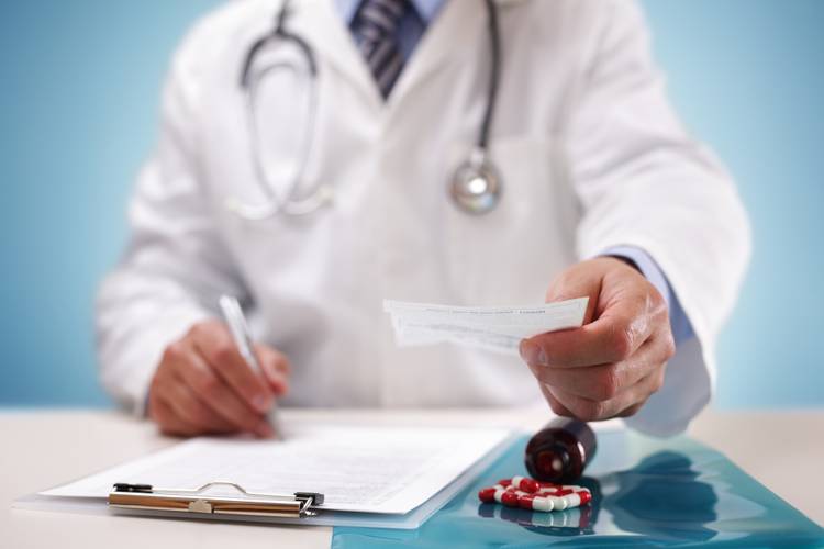 Doctor in a white coat handing a medical prescription to a patient over a clinic desk with pills. Doctor in a white coat handing a medical prescription to a patient over a clinic desk with pills.