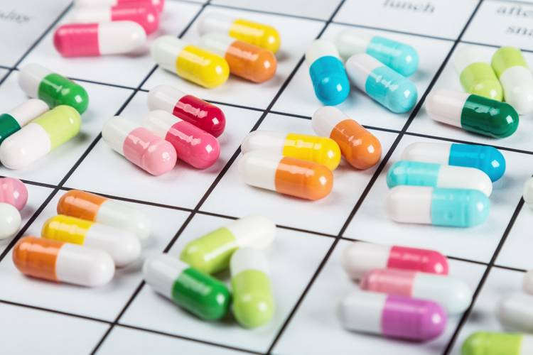 Colorful medical capsules and pills organized on a daily medication schedule grid. Colorful medical capsules and pills organized on a daily medication schedule grid.