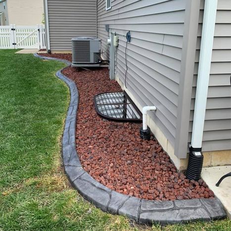 Concrete landscape border defining red rock bed beside house