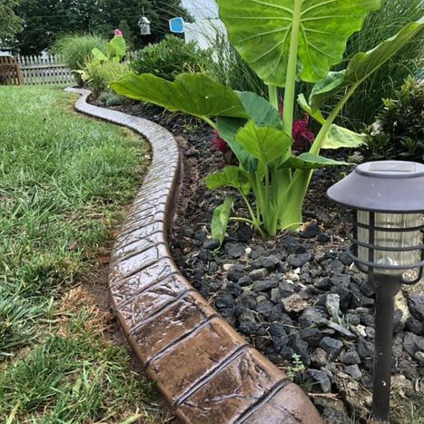 Curved stone landscape border with tropical plants and pathway light