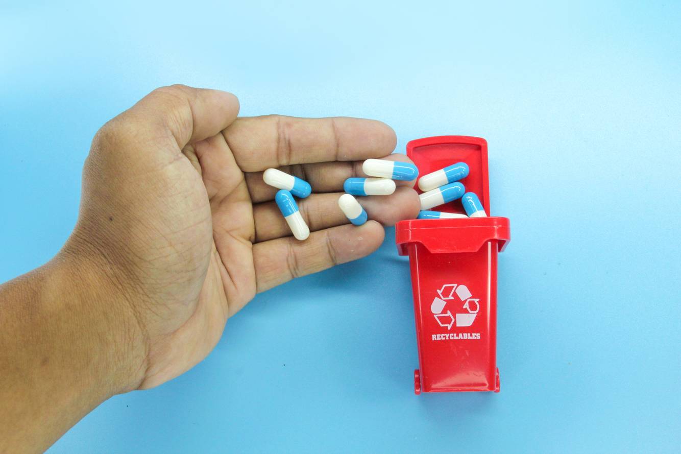 Person throwing away medication in a mini recycle bin Medical waste