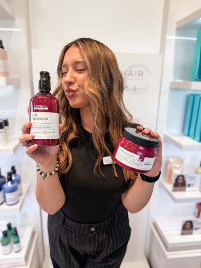 AHC stylist Haley holding L’Oréal Professionnel Curl Expression shampoo and mask at Alexander Hair Creatives in Derry NH. Perfect for hydrating and defining curls with lightweight moisture and shine. L’Oréal Professionnel Curl Expression at Alexander Hair Creatives