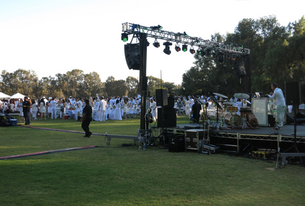 Image of stage at an outdoor event with audience all dressed in white