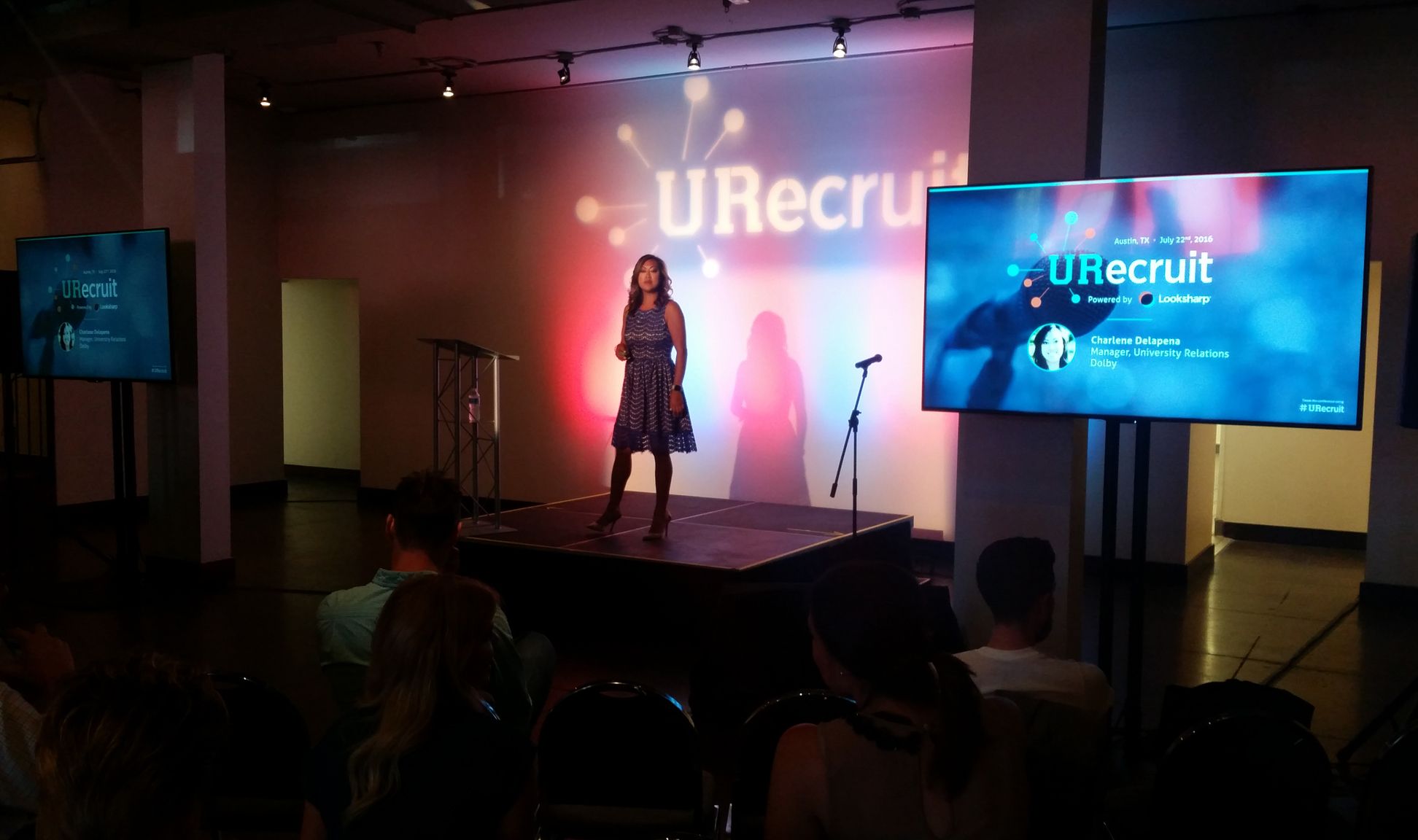 Women speaking on small stage with flat screen monitor display