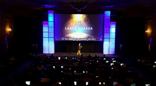 Conference stage with one speaker, large LED display and plexiglass columns with blue lighting 