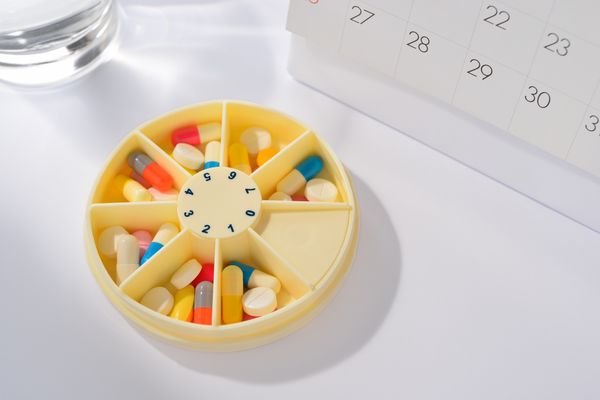 Pills in an organizer sitting next to a calendar Med Sync
