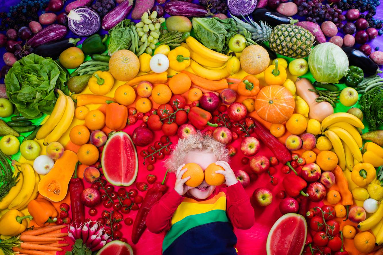kid surrounded by healthy fruits Vitamins for kids