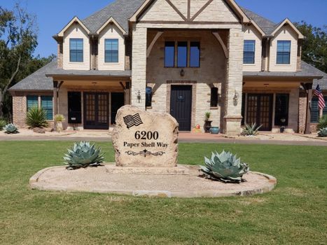 Custom engraved residential address boulder for 6200 Paper Shell Way installed in front yard landscape.