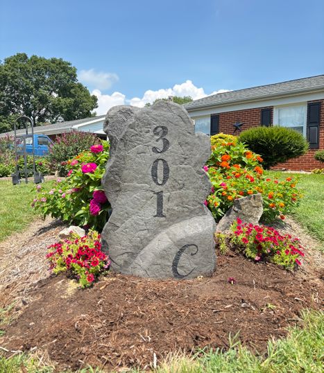 Tall gray engraved stone displaying the house number 301 C surrounded by colorful flowers and front yard landscaping created by Angelopulos StoneCraft