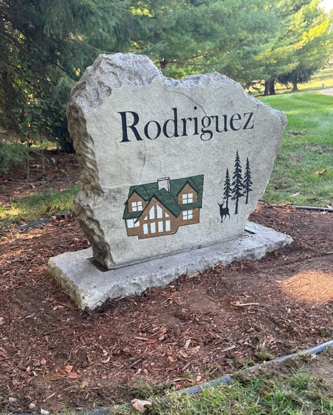 Engraved Rodriguez family stone sign with cabin illustration and pine trees