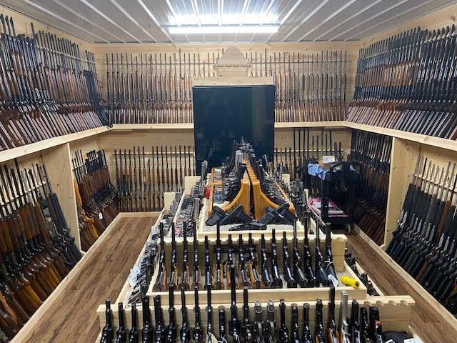 multiple rifles on a gun rack inside a vault room with another gun rack in the middle of the room.