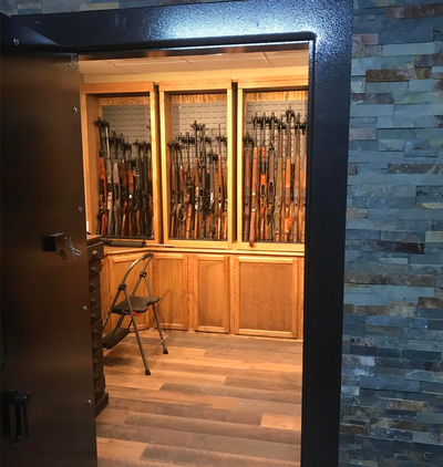 An opened vault door that shows the inside of a vault room that contains gun cabinets filled with different firearms.