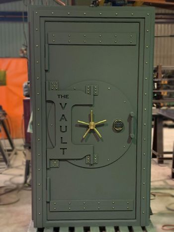 Green steam punk finished vault door with gold rivets, gold handle, and the words The Vault engraved in the front.