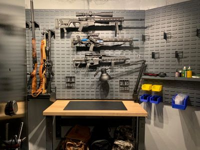 Different assault rifles on a gun wall above a workbench in a vault room.