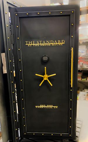 A black vault door with gold text, rivets, and handle with custom text on the front of the door.