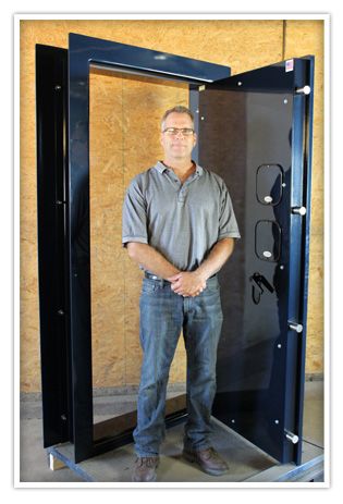Man in collared shirt and blue jeans standing next to an opened, uninstalled vault door.