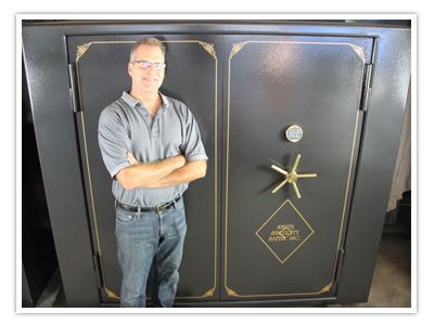 Man in collared shirt and bule jeans standing in front of a double door gun safe. 