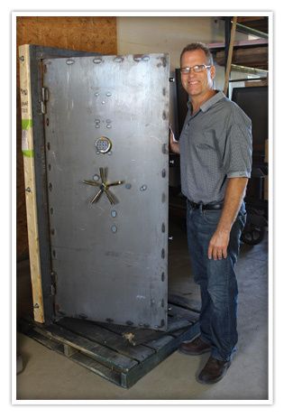 A man in a collared shirt and blue jeans opening up a steel vault door.