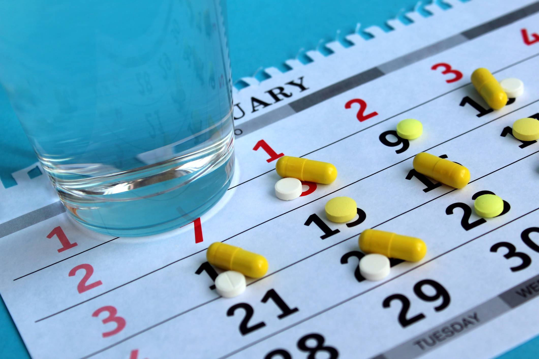 Medicine laying on a calendar with a glass of water Medication Synchronization