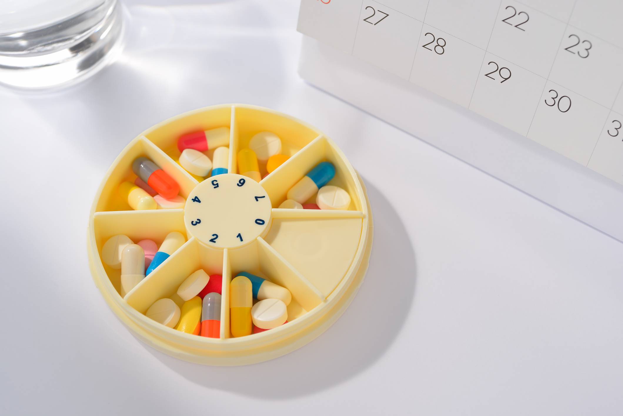 Medications in a pill organizer, sitting next to a calendar. Med Sync