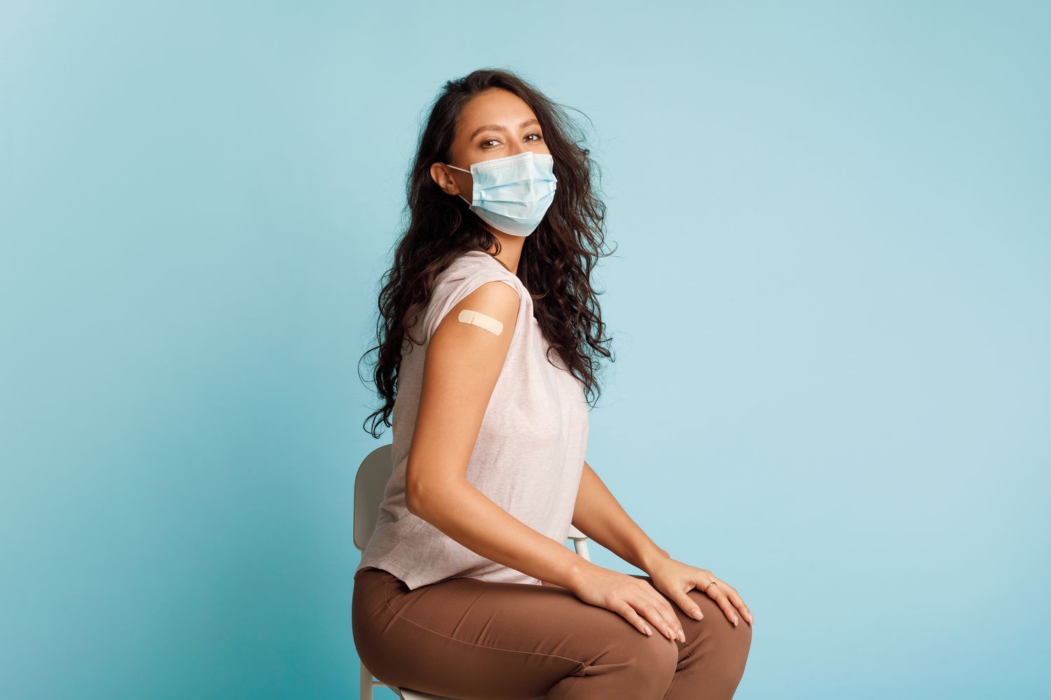 Woman with a bandaid on her upper arm and a mask on. COVID-19 Immunizations