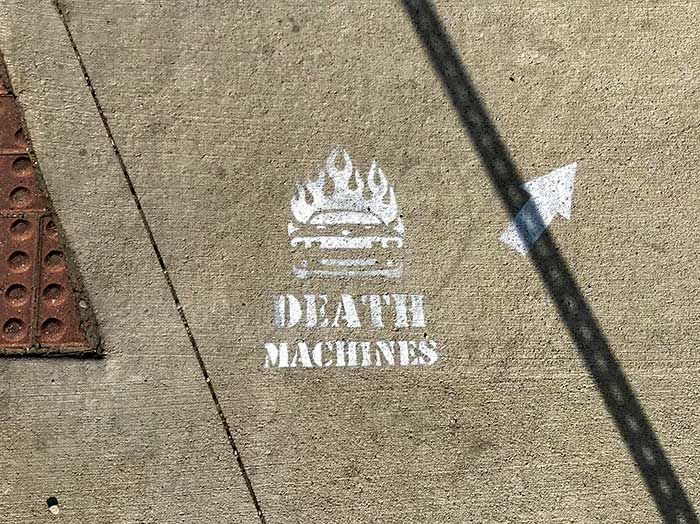 Spray paint on a side walk that has a car on fire and says "death machines" 5