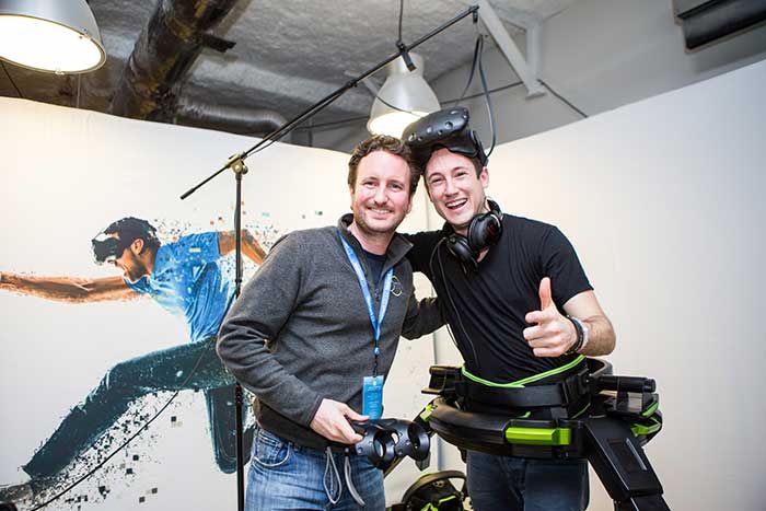 Two guys smiling for the camera. They have VR headsets on their head. 5