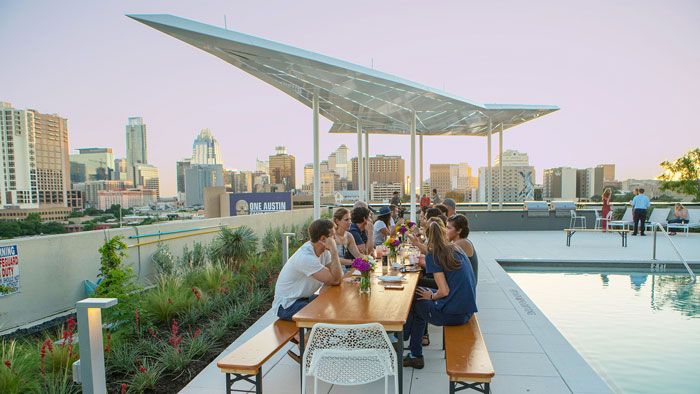 Lond table outside by a pool with a view of Austin. People are sitting at the table eating. 5